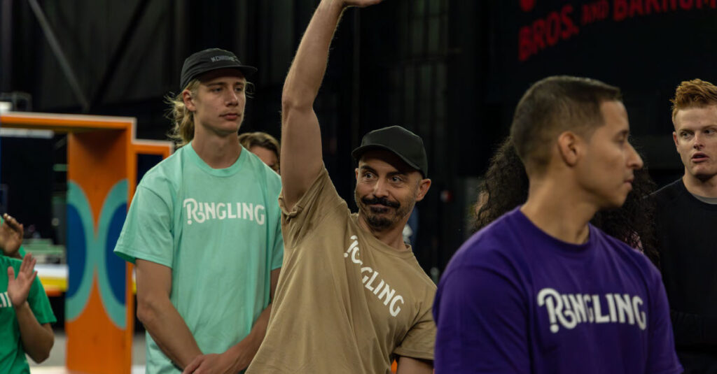 Three Ringling performers standing in a line, with the middle one raising his hand
