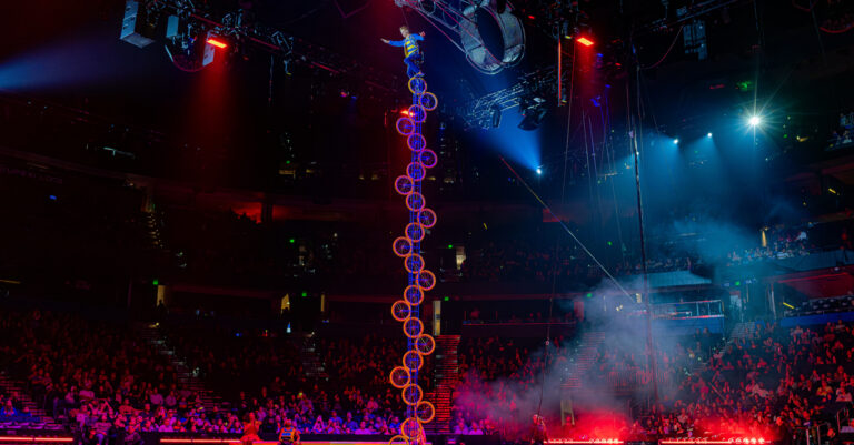 Rider performs on stage on a tall unicycle.